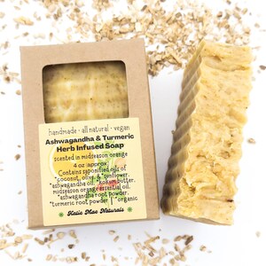 May include: A 4 ounce bar of handmade, all-natural, vegan Ashwagandha & Turmeric Herb Infused Soap, scented in midseason orange. The soap is in a brown cardboard box with a white label. The label lists the ingredients: coconut, olive, sunflower, ashwagandha oil, kokum butter, midseason orange essential oil, ashwagandha root powder, turmeric root powder, and organic.