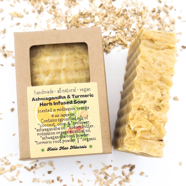 May include: A 4 ounce bar of handmade, all-natural, vegan Ashwagandha & Turmeric Herb Infused Soap, scented in midseason orange. The soap is in a brown cardboard box with a white label. The label lists the ingredients: coconut, olive, sunflower, ashwagandha oil, kokum butter, midseason orange essential oil, ashwagandha root powder, turmeric root powder, and organic.