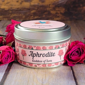 May include: A silver tin candle with a pink label that says "Little Small Hand Poured Soy Wax Candle 6 oz" and "Aphrodite Goddess of Love". The label has a floral pattern with pink roses.