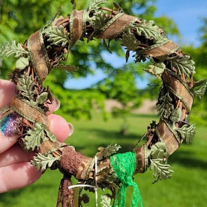Pu&ograve; includere: Una ghirlanda marrone e verde con nastro marrone e foglie verdi. La ghirlanda &egrave; decorata con nastro marrone e verde e ha un nastro verde e marrone che pende dal basso.