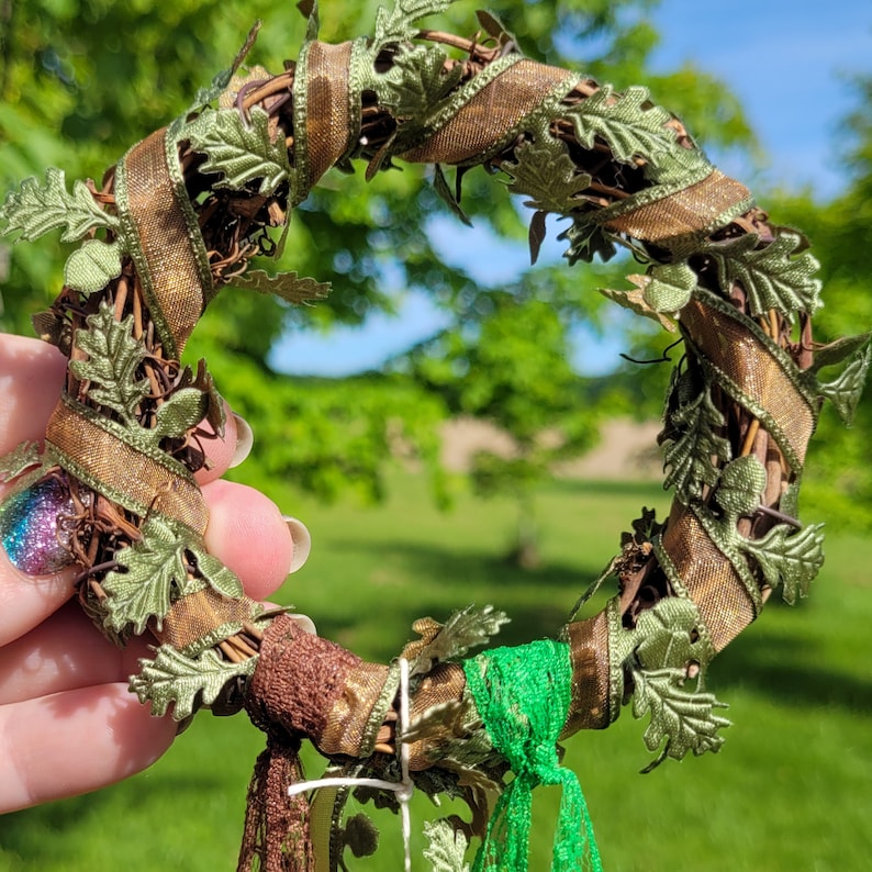 Pu&ograve; includere: Una ghirlanda marrone e verde con nastro marrone e foglie verdi. La ghirlanda &egrave; decorata con nastro marrone e verde e ha un nastro verde e marrone che pende dal basso.
