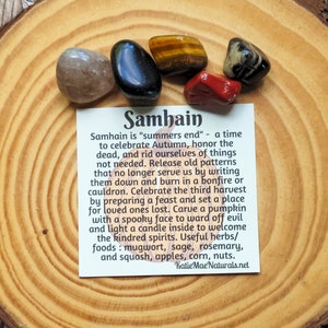 May include: A card with the word "Samhain" written on it, surrounded by various crystals. The card explains the meaning of Samhain, a time to celebrate Autumn, honor the dead, and release old patterns. It also mentions the use of herbs and foods like mugwort, sage, rosemary, squash, apples, corn, and nuts.