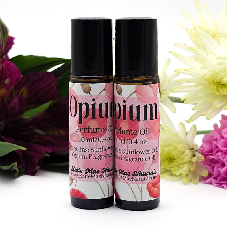 Puede incluir: Dos botellas de aceite de perfume Opium de 10 ml (0,4 oz) con aplicador de bola. Las botellas tienen tapas negras y etiquetas con flores de amapola rosas y el texto "Opiumium Perfume Oil" y "Contains: Sunflower Oil, Opium Fragrance".