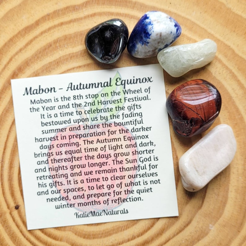 May include: A card with the text "Mabon - Autumnal Equinox" and a description of the holiday. The card is surrounded by six colorful stones, including black, blue, white, red, and pink.