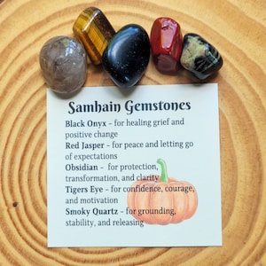 May include: A set of six polished gemstones with a card that reads "Samhain Gemstones" and lists the names and properties of each stone: Black Onyx, Red Jasper, Obsidian, Tigers Eye, and Smoky Quartz.