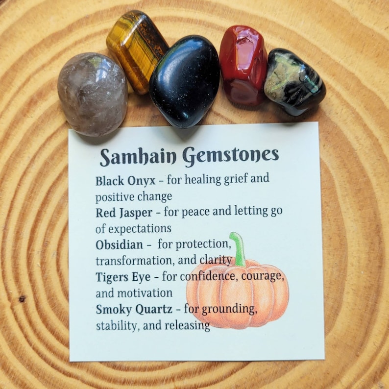 May include: A set of six polished gemstones with a card that reads "Samhain Gemstones" and lists the names and properties of each stone: Black Onyx, Red Jasper, Obsidian, Tigers Eye, and Smoky Quartz.