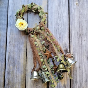 May include: A brown and green wreath with a white flower and brown ribbon. The wreath is decorated with bells and stars.