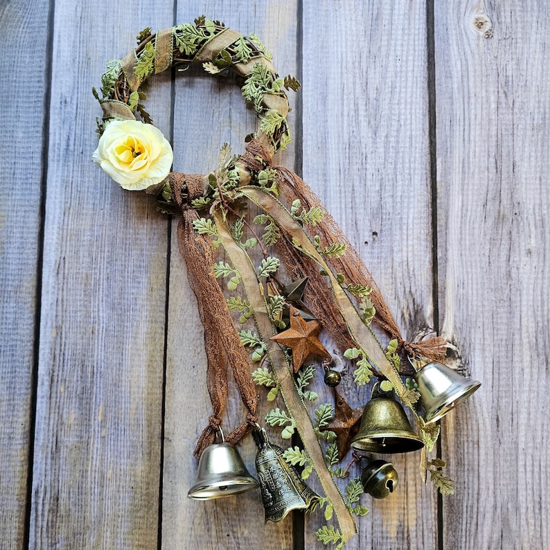 May include: A brown and green wreath with a white flower and brown ribbon. The wreath is decorated with bells and stars.