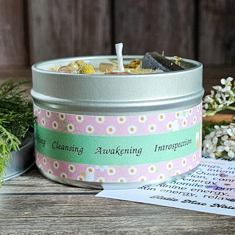 May include: A silver tin candle with a white wick and a green, pink, and white label. The label reads "Cleansing Awakening Introspection".