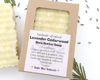 May include: A bar of handmade, all-natural lavender and cedarwood shea butter soap in a brown cardboard box. The soap is 4 ounces and contains coconut, olive, sunflower, and grapeseed oils, shea butter, beeswax, arrowroot powder, kaolin clay, lavender, and cedarwood essential oils. The label reads "Katie Mae Naturals".