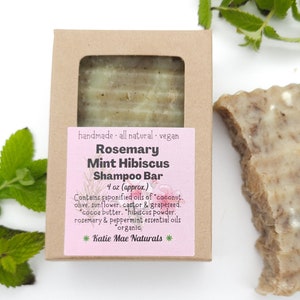 Może przedstawiać: Brązowe pudełko kartonowe z r&oacute;żową etykietą, na kt&oacute;rej widnieje napis: "Rosemary Mint Hibiscus Shampoo Bar 4 oz (approx.) Contains saponified oils of "coconut, olive, sunflower, castor & grapeseed. "cocoa butter. "hibiscus powder. rosemary & peppermint essential oils organic * Katie Mae Naturals *"