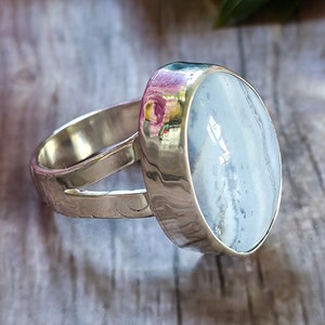 May include: A silver ring with a light blue oval gemstone set in a bezel setting. The band is textured and has a split shank.