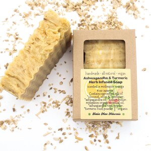 May include: A 4 ounce bar of handmade, all-natural, vegan ashwagandha and turmeric herb infused soap, scented in midseason orange. The soap is in a brown cardboard box with a label that lists the ingredients: coconut, olive, sunflower, ashwagandha oil, kokum butter, midseason orange essential oil, ashwagandha root powder, turmeric root powder, and organic. The label also includes the brand name "Katie Mae Naturals".
