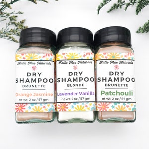 May include: Three small glass jars with white lids containing dry shampoo for different hair colors. The jars are labeled "Katie Mae Naturals Dry Shampoo" with the hair color and scent listed below. The scents are Orange Jasmine, Lavender Vanilla, and Patchouli.