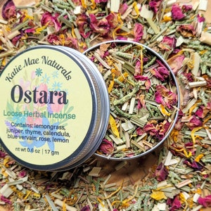 May include: A silver tin with a yellow label that reads "Katie Mae Naturals Ostara Loose Herbal Incense". The label also lists the ingredients: lemongrass, juniper, thyme, calendula, blue vervain, rose, and lemon. The tin is open and filled with a blend of dried herbs and flowers, including lemongrass, rose petals, and calendula.
