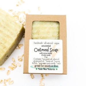 May include: A brown cardboard box with a clear window showing a green bar of oatmeal soap. The label reads "handmade all natural. vegan unscented Oatmeal Soap with cocoa butter & zinc oxide 4 oz Contains: "coconut oil, olive oil. grapeseed oil. hemp oil. cocoa butter. "non nano zinx oxide. "oats great for sensitive skin! *Katie Mae Naturals *"