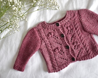 May include: A pink knitted cardigan with a cable knit pattern and buttons down the front.