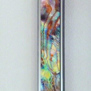 Puede incluir: Una impresión de arte abstracto enmarcada que presenta colores iridiscentes azules, verdes y naranjas. La impresión está enmarcada en un marco negro con un passe-partout blanco.