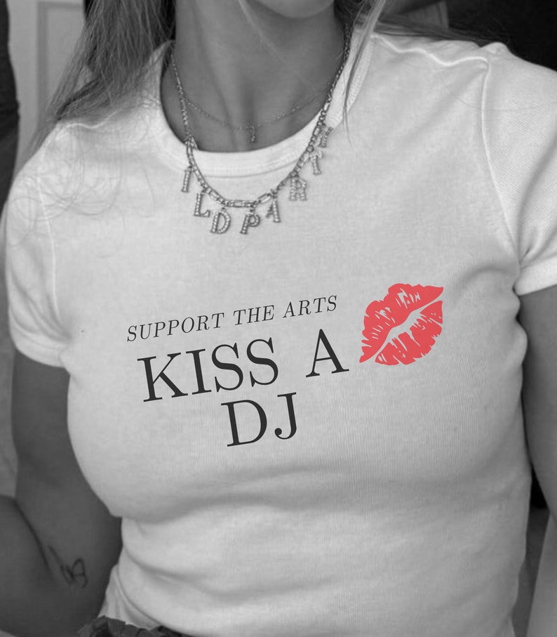 Puede incluir: Camiseta blanca con el texto "Support the Arts Kiss a DJ" y una impresi&oacute;n de labios rojos.