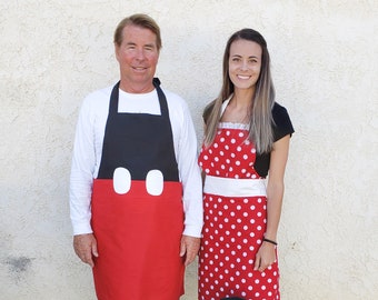 May include: A family and their dog are wearing matching aprons. The aprons are red with white polka dots and a white bow. The man's apron is designed to look like Mickey Mouse. The dog is wearing a matching dress.