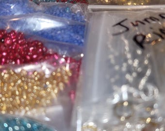 May include: Assortment of jewelry-making supplies, including colorful beads and metal charms, stored in clear plastic bags. The bags are labeled with handwritten text, and the beads come in various colors.
