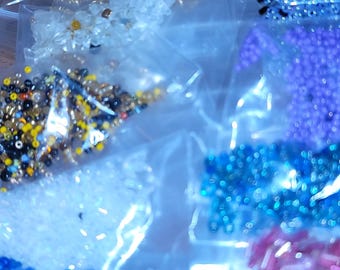 May include: Assortment of small, colorful beads in clear plastic bags. The beads are in various colors, including gold, blue, purple, and pink. Ideal for jewelry making and crafting projects.