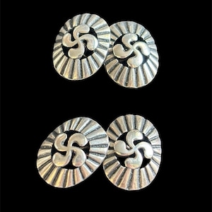 May include: Four oval-shaped silver-toned metal buttons featuring a central cutout design of a four-armed curved cross. Each button has a radiating sunburst pattern around the center, with a polished finish and dark recessed areas.