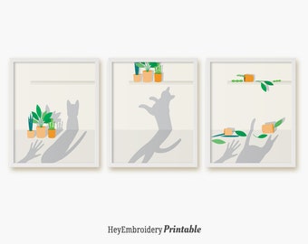 May include: Three framed prints with a white background and a white frame. The prints feature a silhouette of a cat jumping, a cat sitting, and a cat with its paws up in the air. Each print has a shelf with potted plants on it.