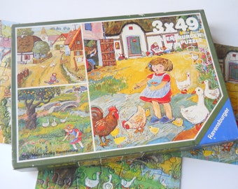 May include: A Ravensburger 3x49 piece jigsaw puzzle box featuring a colorful illustration of a rural farm scene. The artwork depicts a child feeding chickens and geese in a yard with houses, trees, and a stone bridge. The box has green borders.