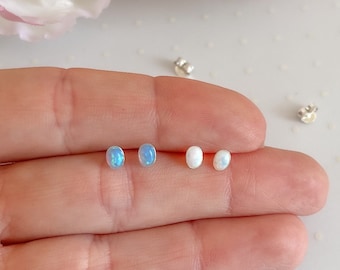 Puede incluir: Cuatro pendientes de plata con piedras de ópalo de forma ovalada. Dos pendientes tienen una piedra de ópalo azul claro, y dos pendientes tienen una piedra de ópalo blanca.