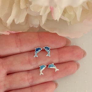 May include: A pair of silver dolphin stud earrings with blue enamel. The dolphins are facing opposite directions and have a gradient of blue enamel.