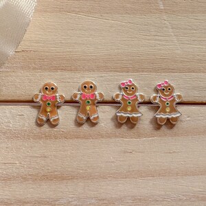 May include: Four gingerbread person charms, two with pink bows and two with red bow ties. The charms are silver with brown, white, pink, red, and green enamel details.