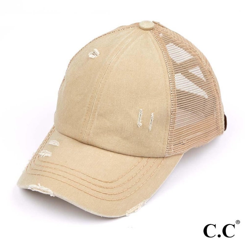 May include: Tan baseball cap with a distressed, worn look. The cap features a mesh back for breathability and a curved brim. The front of the cap has a few small holes. The brand logo "C.C." is visible on the bottom right.