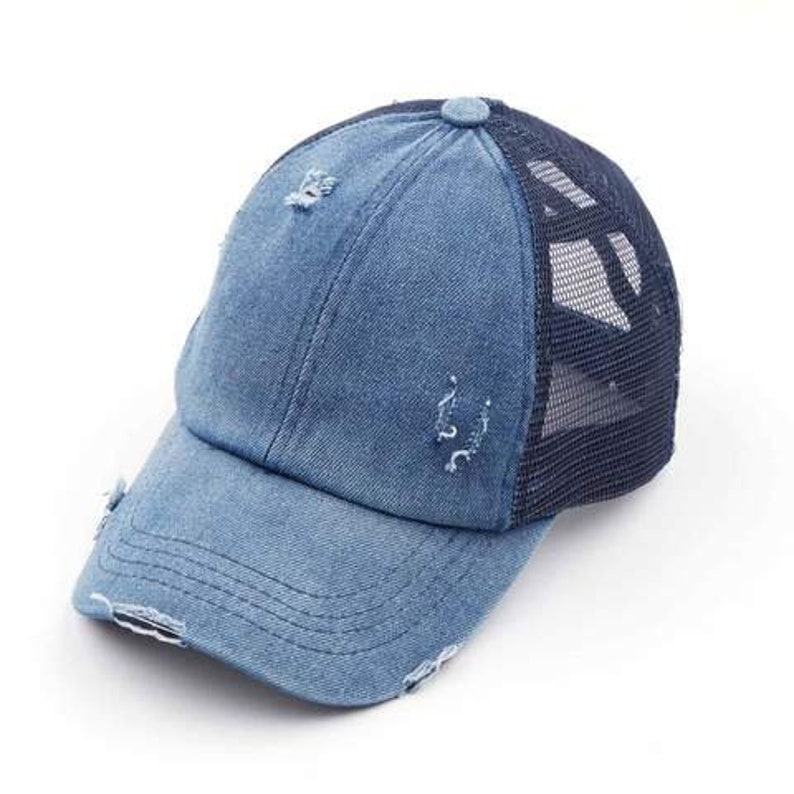 May include: A blue denim baseball cap with a distressed, worn look. The cap features a mesh back and a curved brim. The denim has intentional rips and tears, giving it a vintage aesthetic. A button detail sits atop the crown.