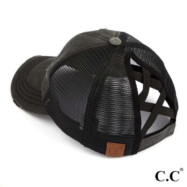 May include: Distressed black baseball cap with a mesh back and crisscross elastic detail. The cap features a curved brim and a small, round button on top. A brown leather patch with "C.C." is visible on the side.