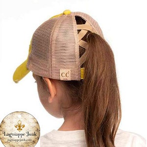 May include: Tan and yellow CC brand ponytail baseball cap. The cap features a mesh back, a yellow bill, and a criss-cross design for a ponytail. The CC logo is visible on the side.