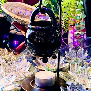 Peut inclure: Brûleur de cire noire en forme de chaudron avec un support en métal et une bougie chauffe-plat. Le brûleur est entouré de décorations en verre transparent en forme de lotus.