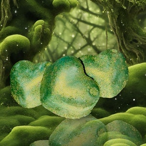 Peut inclure: Trois ornements en forme de cœur vert avec des paillettes dorées suspendus dans un décor de forêt mousseuse.