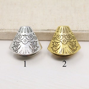 May include: Two metal decorative end caps with an intricate design. The end cap on the left is silver and the end cap on the right is gold.