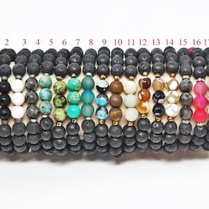 May include: A collection of beaded bracelets, each featuring a combination of black lava rock beads and accent beads in various colors and materials. The accent beads include blue, white, green, and brown stones, as well as other colorful beads. The bracelets are displayed on a neutral fabric.