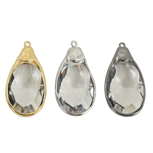 May include: Three teardrop-shaped pendants with clear, faceted crystal stones. The pendants have different metal finishes: gold, silver, and gunmetal. Each pendant has a small loop at the top for attaching to a chain or other jewelry component.