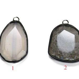 May include: Three agate pendants with black metal frames. The first pendant is white, the second is gray with brown markings, and the third is brown with white markings.