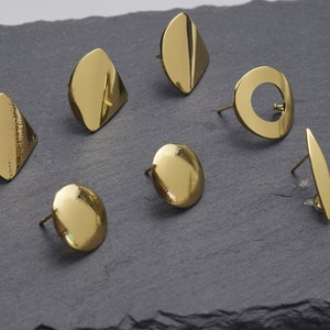 May include: A set of ten gold-toned earrings with various geometric shapes, including circles, ovals, and triangles. The earrings are displayed on a dark gray surface.