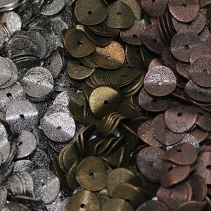 May include: Assortment of metal buttons in various colors, including gold, silver, bronze, and copper. The buttons are all round with a small hole in the center. They are arranged in rows in a container.