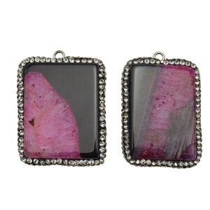 May include: Two rectangular agate pendants with a silver frame and clear crystal accents. The agate is pink and black with a swirling pattern.