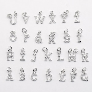 Puede incluir: Un conjunto de 26 abalorios de letras plateadas, cada letra está incrustada con diamantes de imitación transparentes. Los abalorios están dispuestos en orden alfabético.