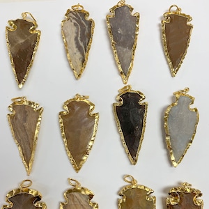 May include: Twelve gold-rimmed arrowhead pendants made of natural stone. Each pendant has a unique pattern and color variation.