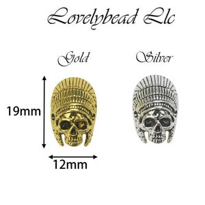 May include: Gold and silver-colored skull-shaped beads, each with a headdress design. The gold bead measures 19mm in height and 12mm in width. The silver bead is next to the gold bead. The text "Lovelybead Llc" is at the top.