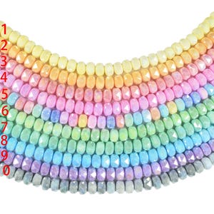 Könnte beinhalten: Eine Sammlung farbenfroher Edelsteinperlen, die in einem Regenbogen-Farbverlauf angeordnet sind. Die facettierten Perlen reflektieren das Licht und reichen von Gelb bis Grau. Die Perlen sind aufgereiht und bilden eine lebendige Darstellung. Jede Perle misst ca. 0,5 cm.