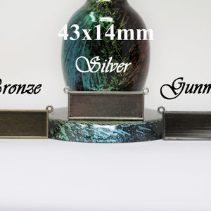 May include: Three rectangular metal blanks for jewelry making in bronze, silver, and gunmetal. Each blank measures 43x14mm.